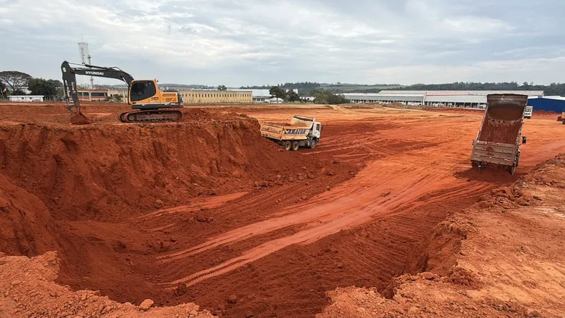 Escavadeira hidráulica carregando caminhão basculante com material escavado — Empolamento do solo: por que o m³ do projeto não é o m³ do caminhão